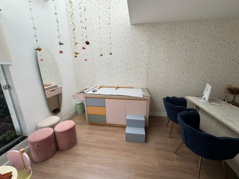 Sala de trocador infantil, com decoração lúdica e poltronas de espera ao fundo
