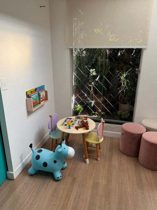 Cantinho lúdico com mesinha infantil, livros e brinquedos, com vista para o jardim