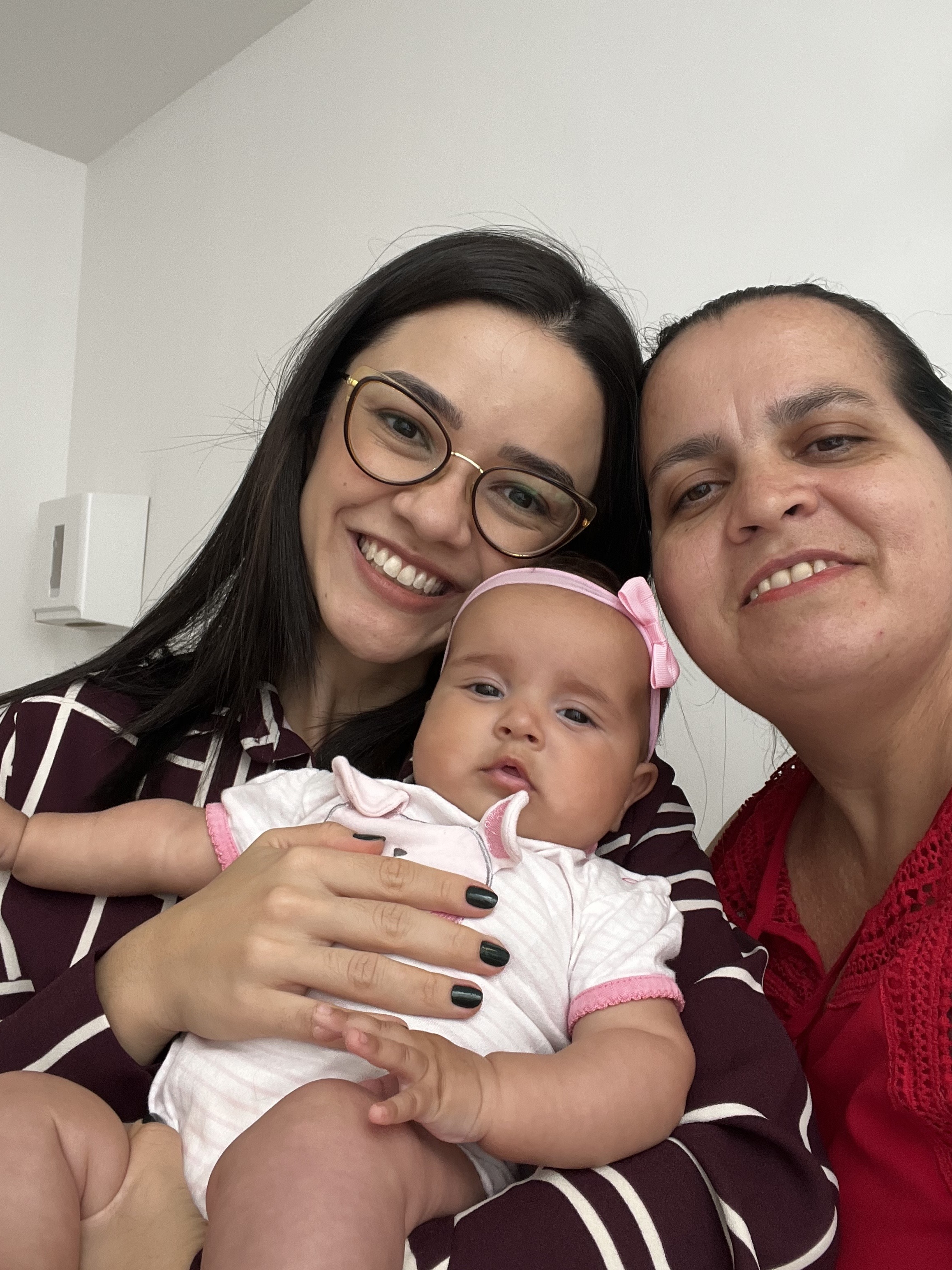 Dra. Andressa sorrindo com uma família e um bebê no consultório